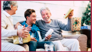 family holiday with woman, son, and older man on couch exchanging gifts by a tree - Neighborly Home Care Senior Companionship